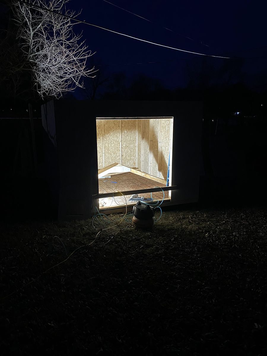 A shed is lit up at night with a light coming out of the door.