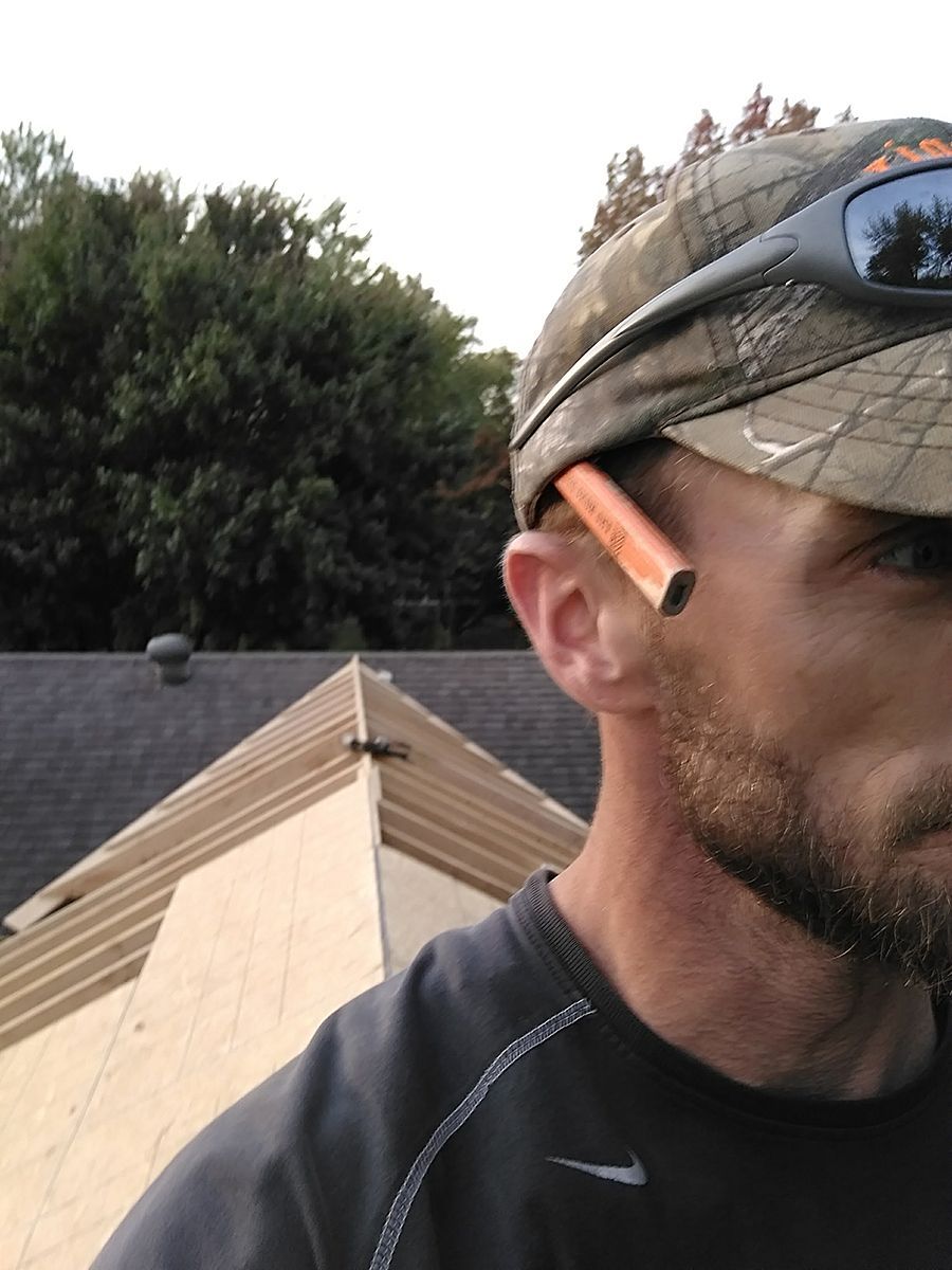 A man wearing a hat and sunglasses is standing in front of a roof.