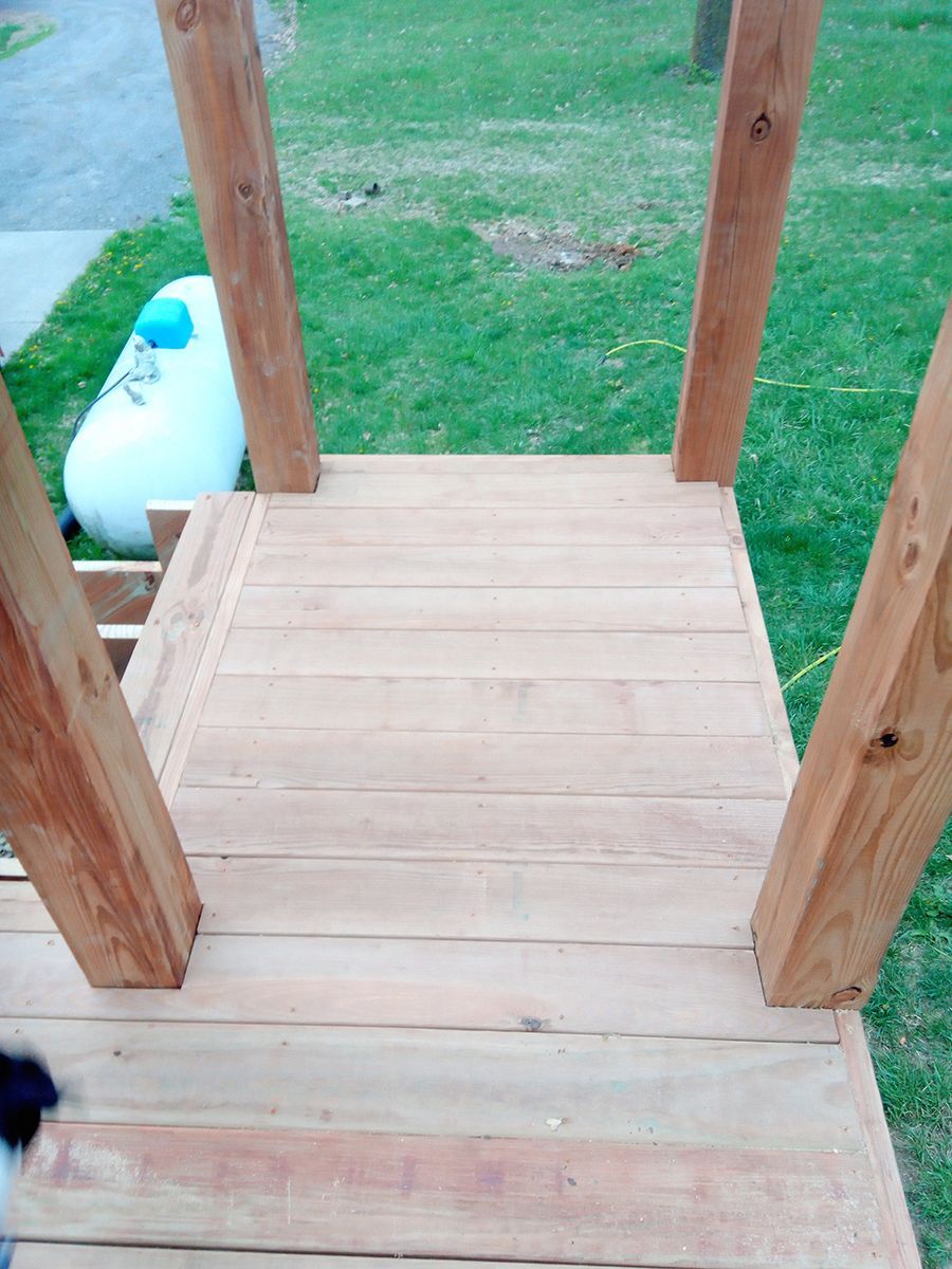 A dog is standing on a wooden deck next to a propane tank.