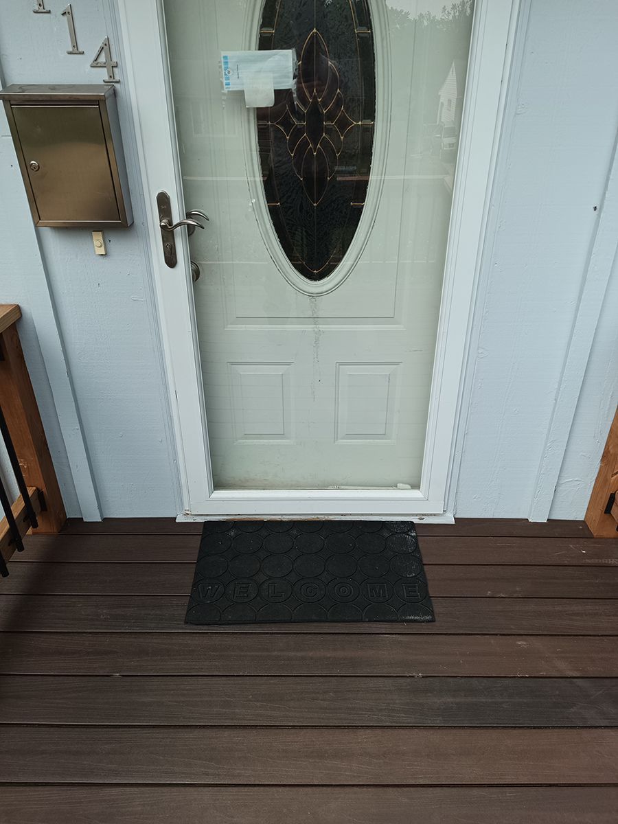 A white door with a stained glass window is on a wooden deck.