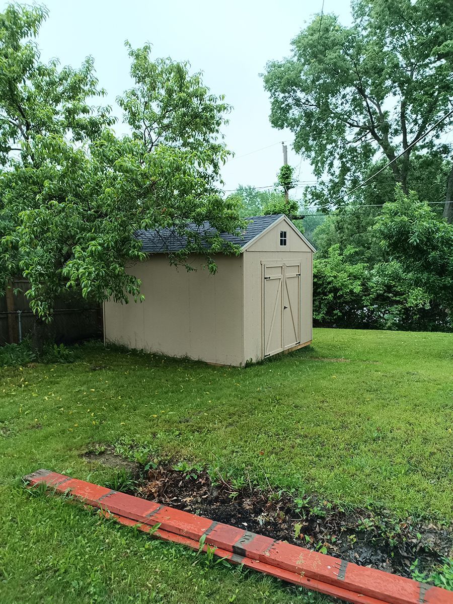A small shed is sitting in the middle of a lush green yard.