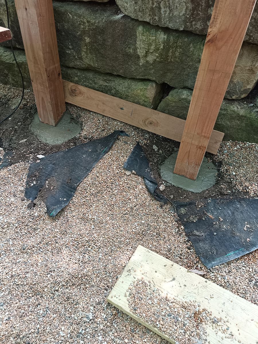 A wooden post is sitting on top of a pile of gravel next to a stone wall.
