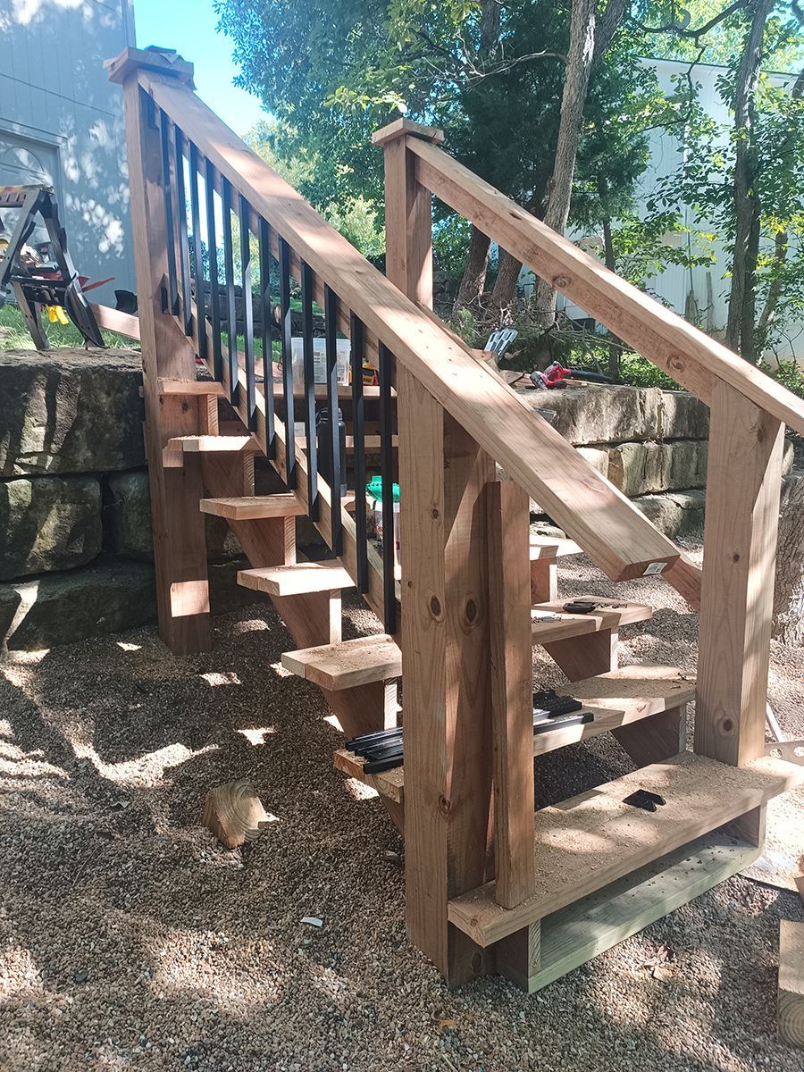 A wooden staircase with a metal railing is sitting on top of a gravel area.