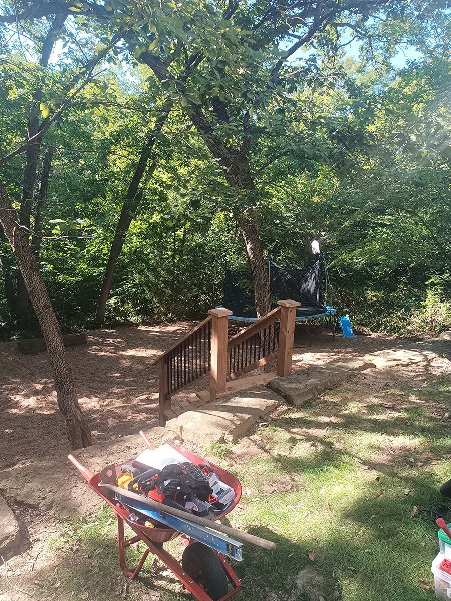 A wheelbarrow filled with tools is sitting in the grass in front of a wooden deck.