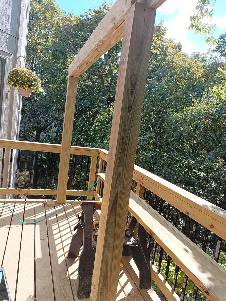 A wooden deck with a bench and trees in the background.