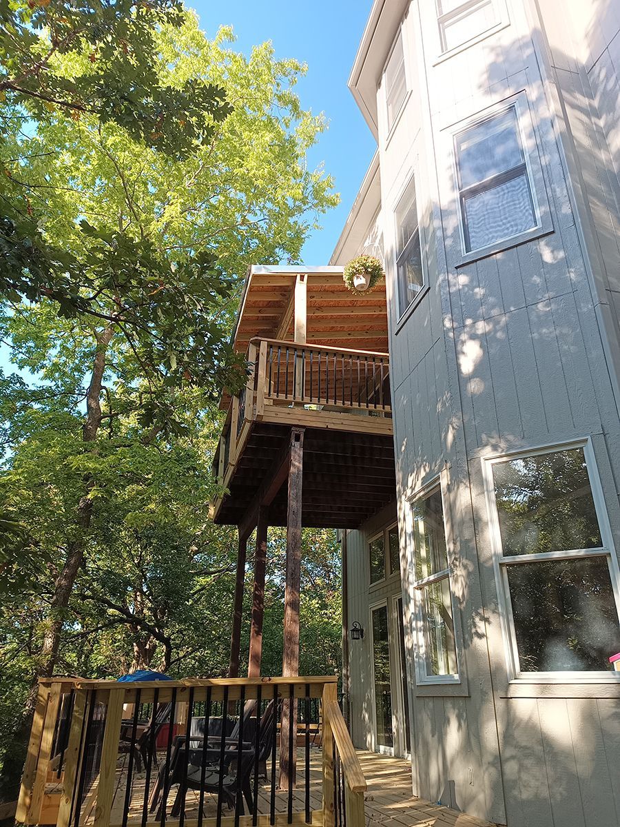 The back of a house with a deck and trees in the background.