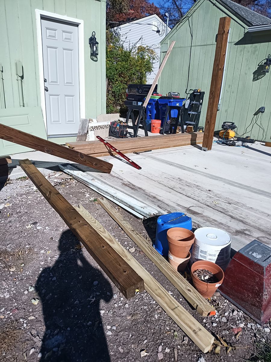 A pile of wood is laying on the ground in front of a green house.