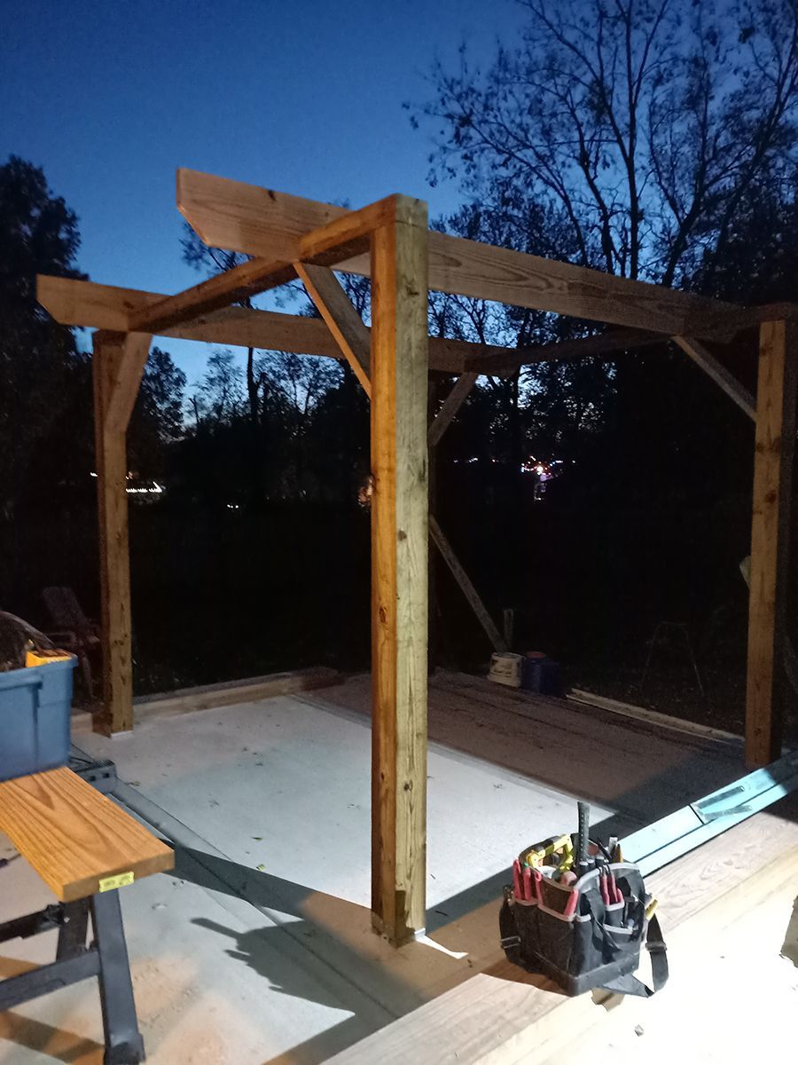 A wooden structure is being built at night with trees in the background.