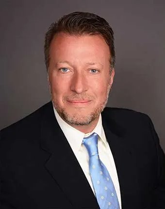 Man in a suit and blue tie smiles at the camera.