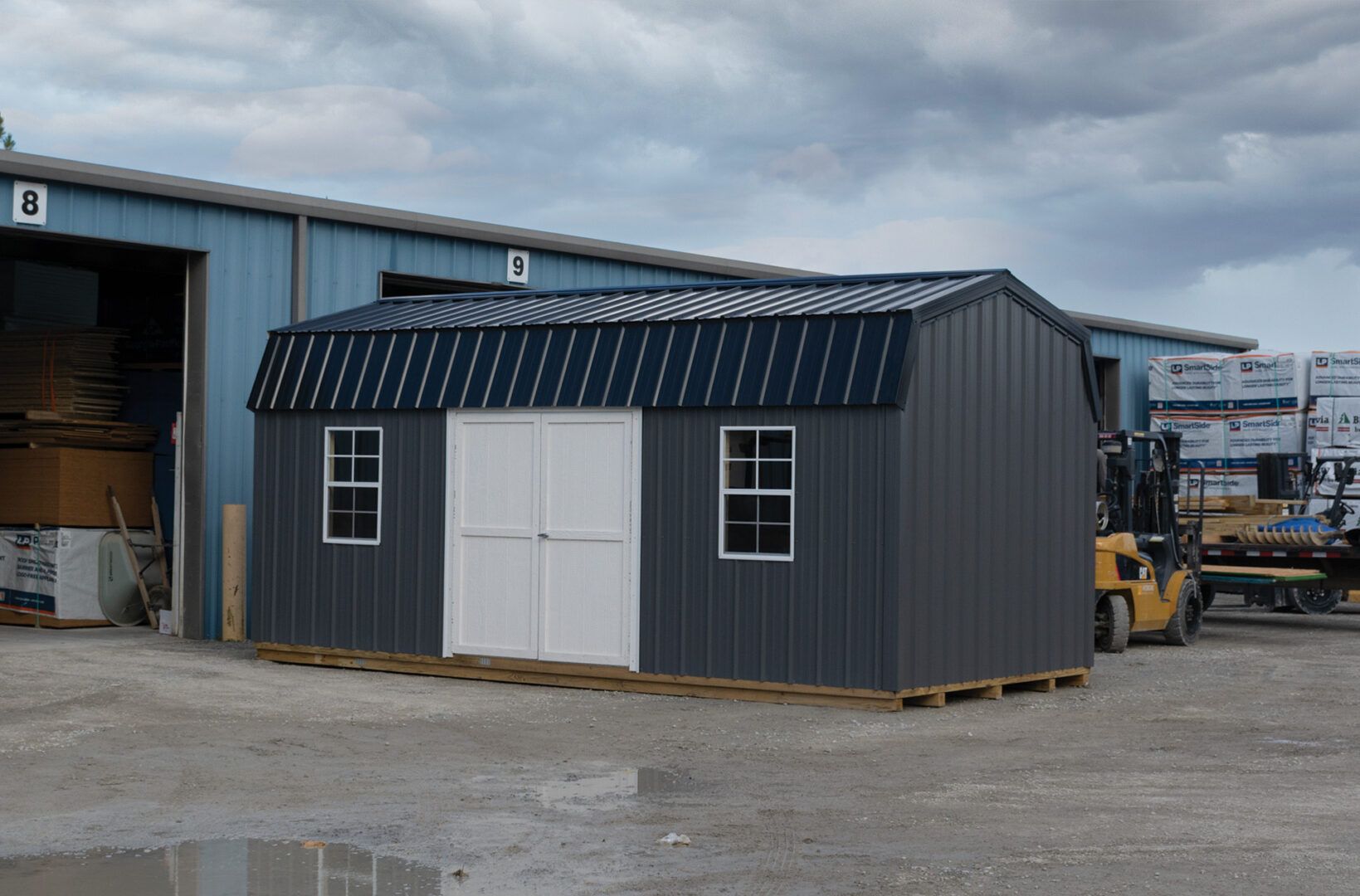 A gray shed with a black roof is sitting in front of a blue building.
