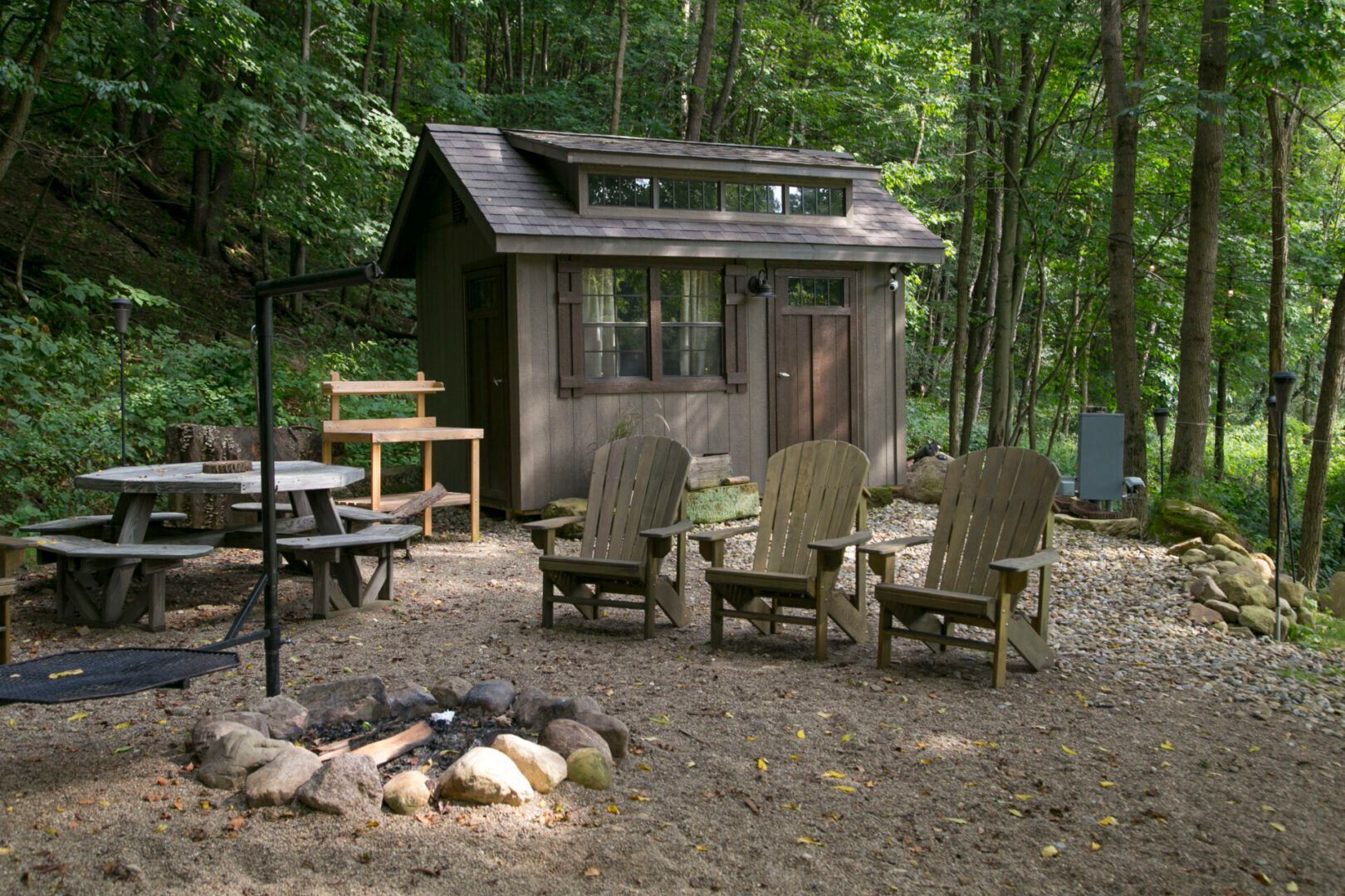 A small cabin in the woods with a fire pit and chairs