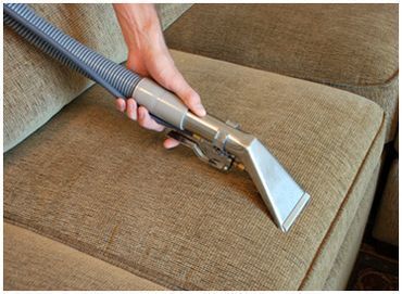 A person is cleaning a couch with a vacuum cleaner.