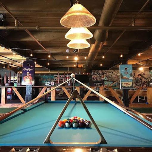 Pool table set for play in a dimly lit bar with hanging lights and exposed beams.