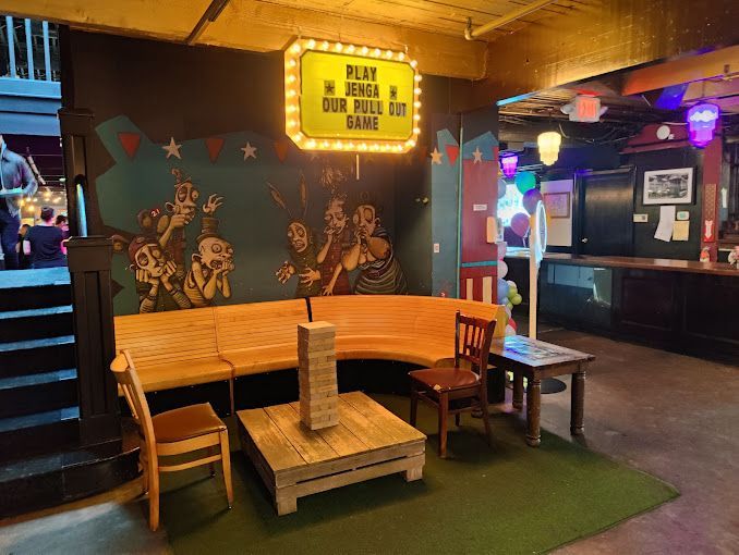 A lounge with wooden benches, a giant Jenga game, and a neon sign that reads