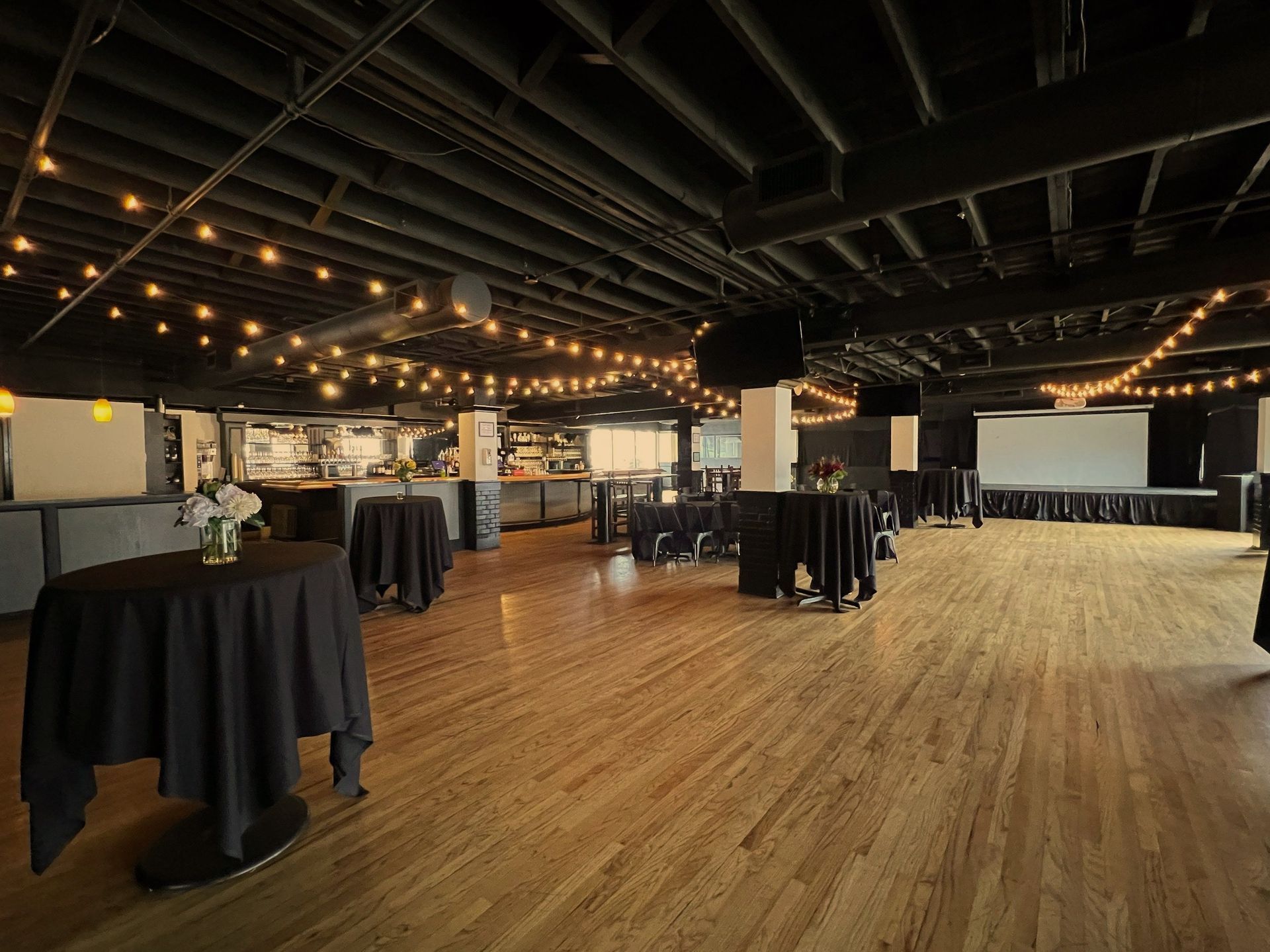 A large room with wooden floors and tables and a projector screen.