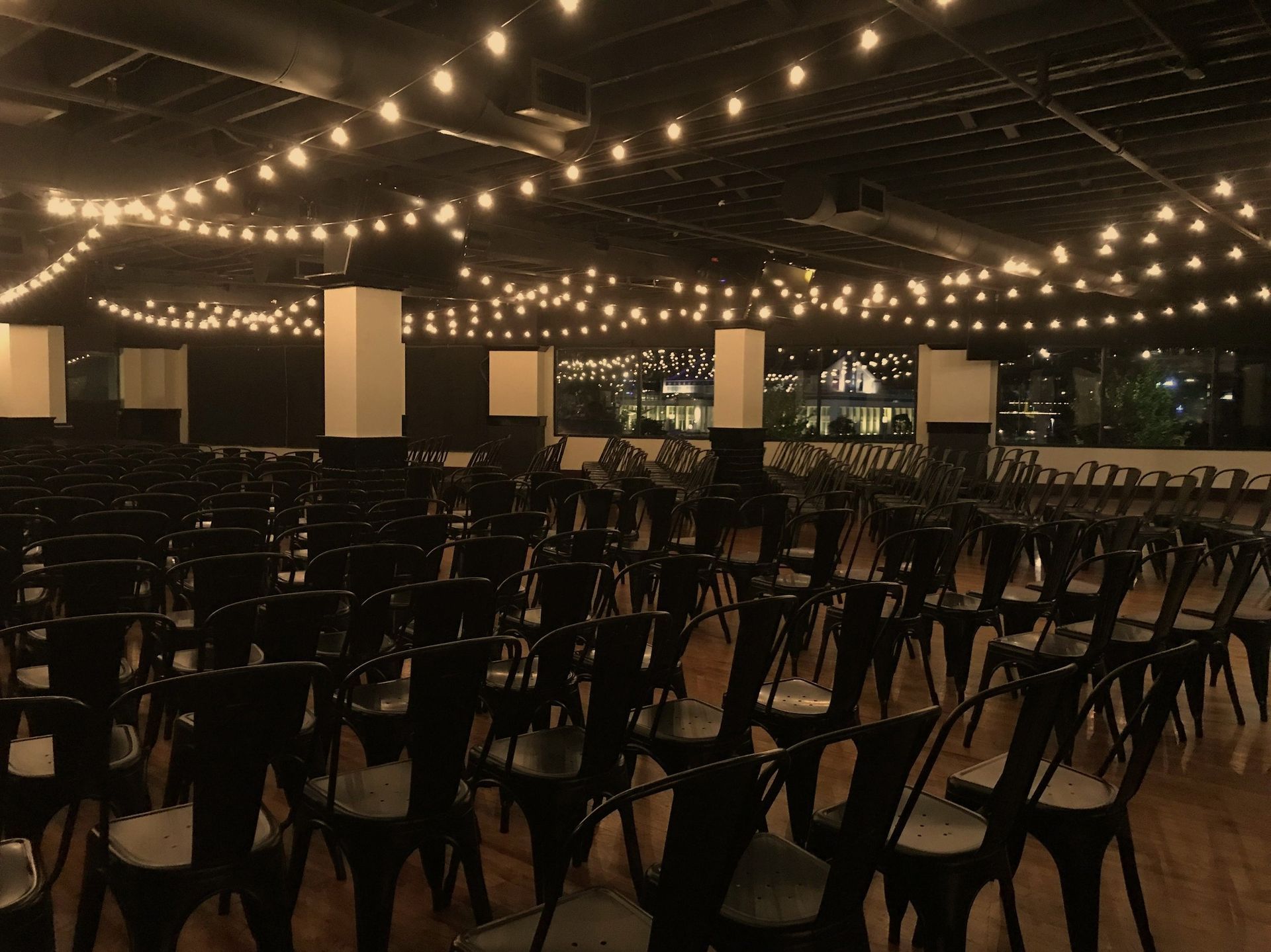 A large room with rows of chairs and string lights hanging from the ceiling.