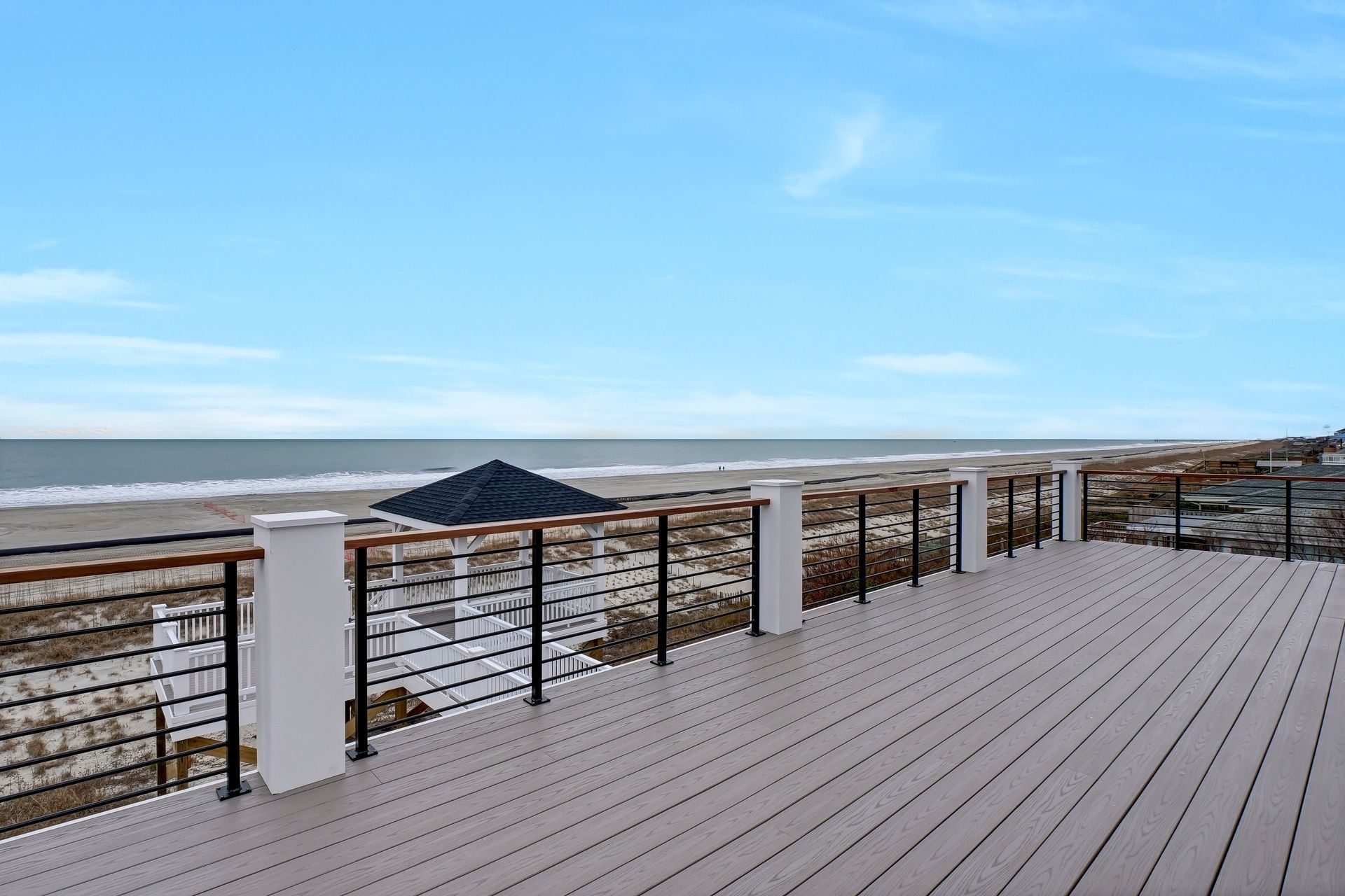 Wooden deck overlooking a beach and ocean under a blue sky.