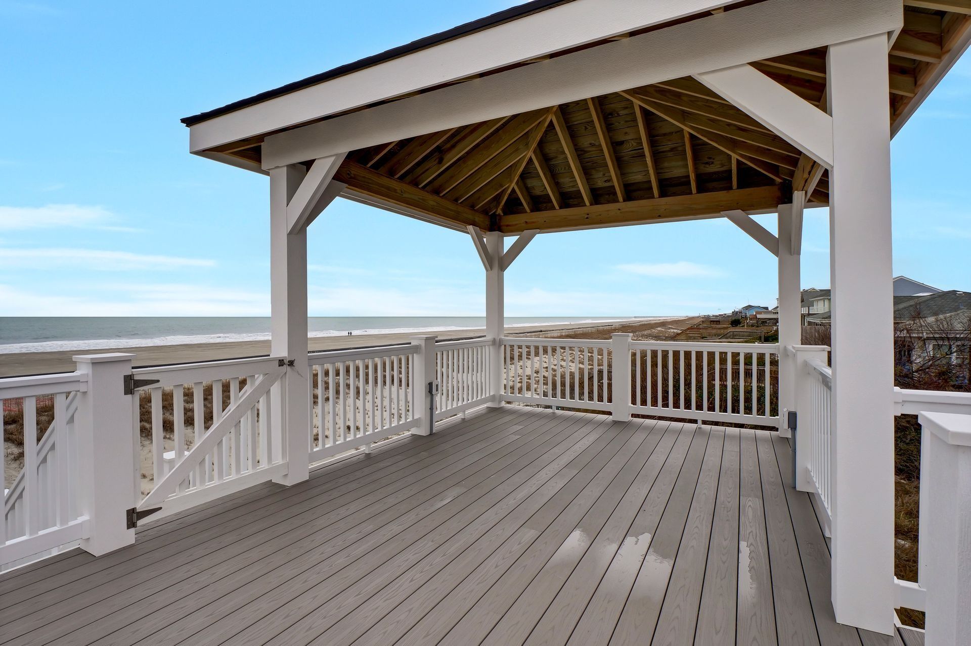 Wooden gazebo on deck overlooking beach, blue sky.