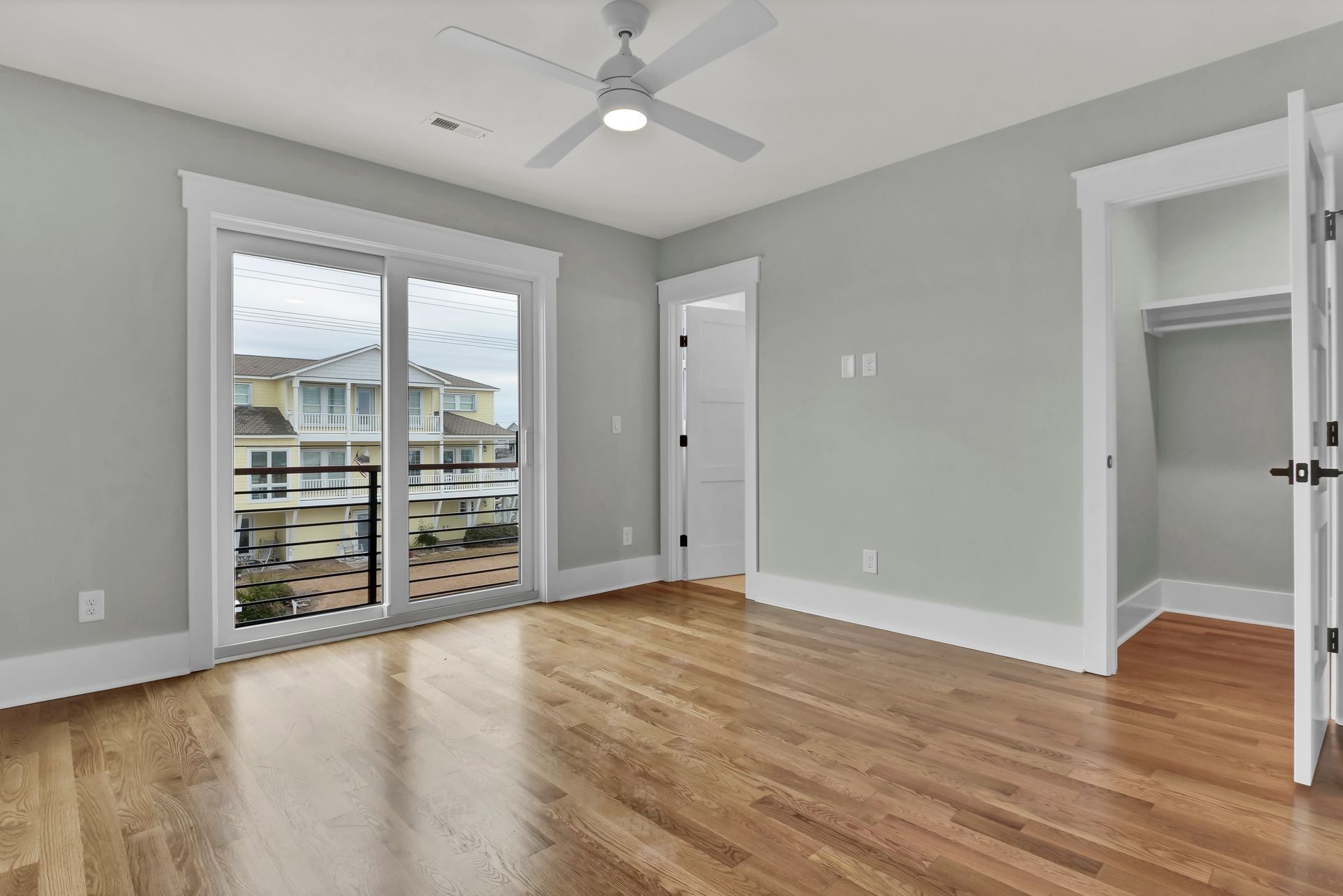 Bedroom with hardwood floors, sliding glass door to balcony, light gray walls, white trim and ceiling fan.