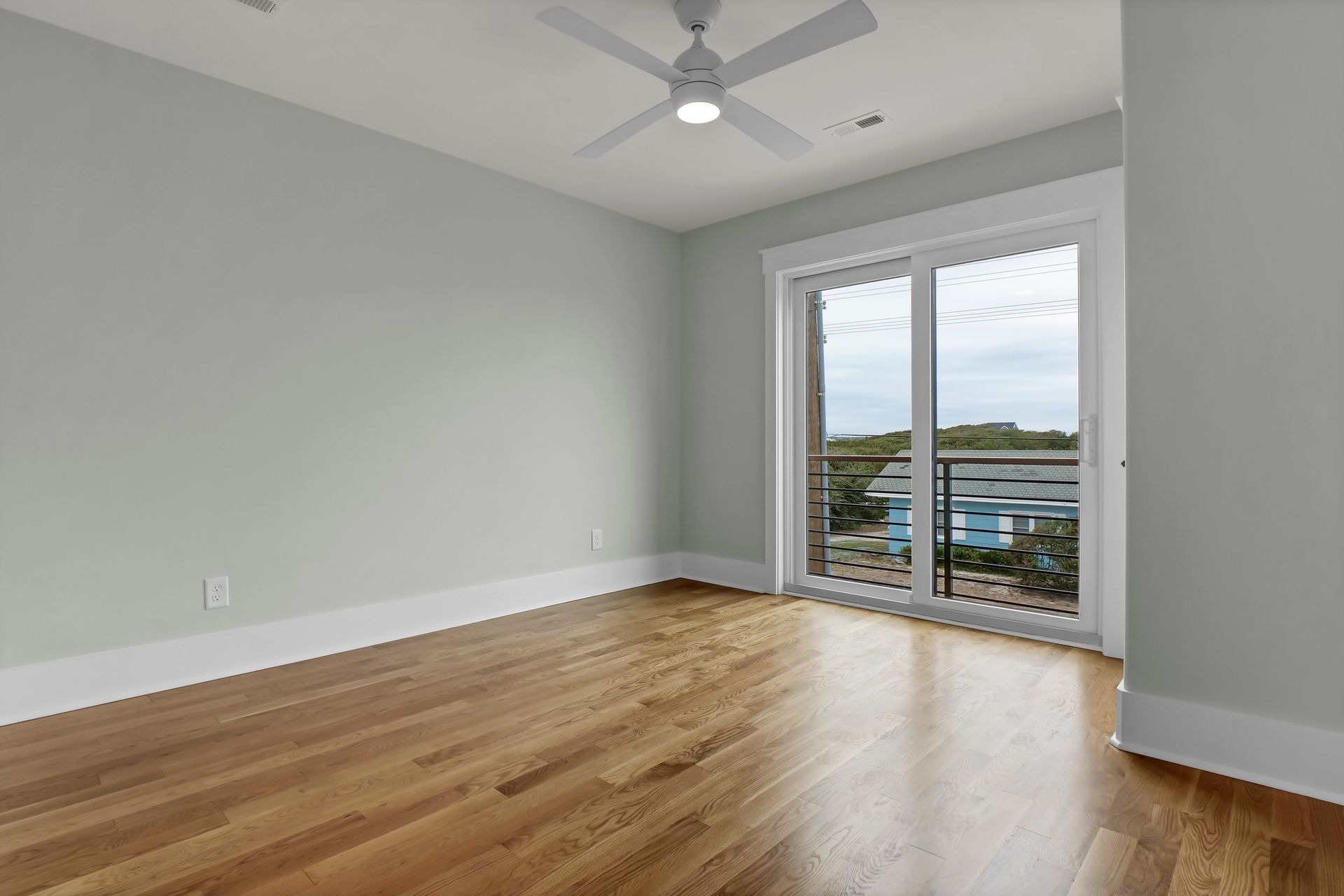 Empty bedroom with light blue walls, hardwood floor, and balcony access.