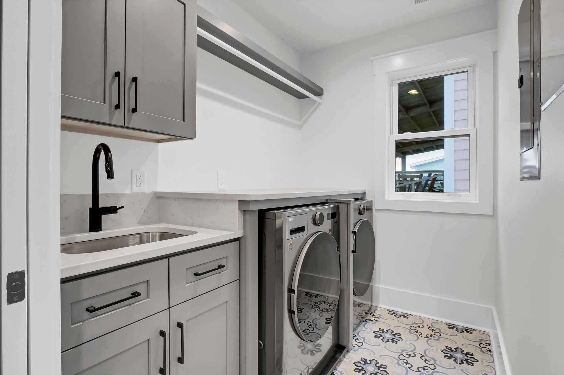 Laundry room with gray cabinets, washer/dryer, sink, and floral tile floor.