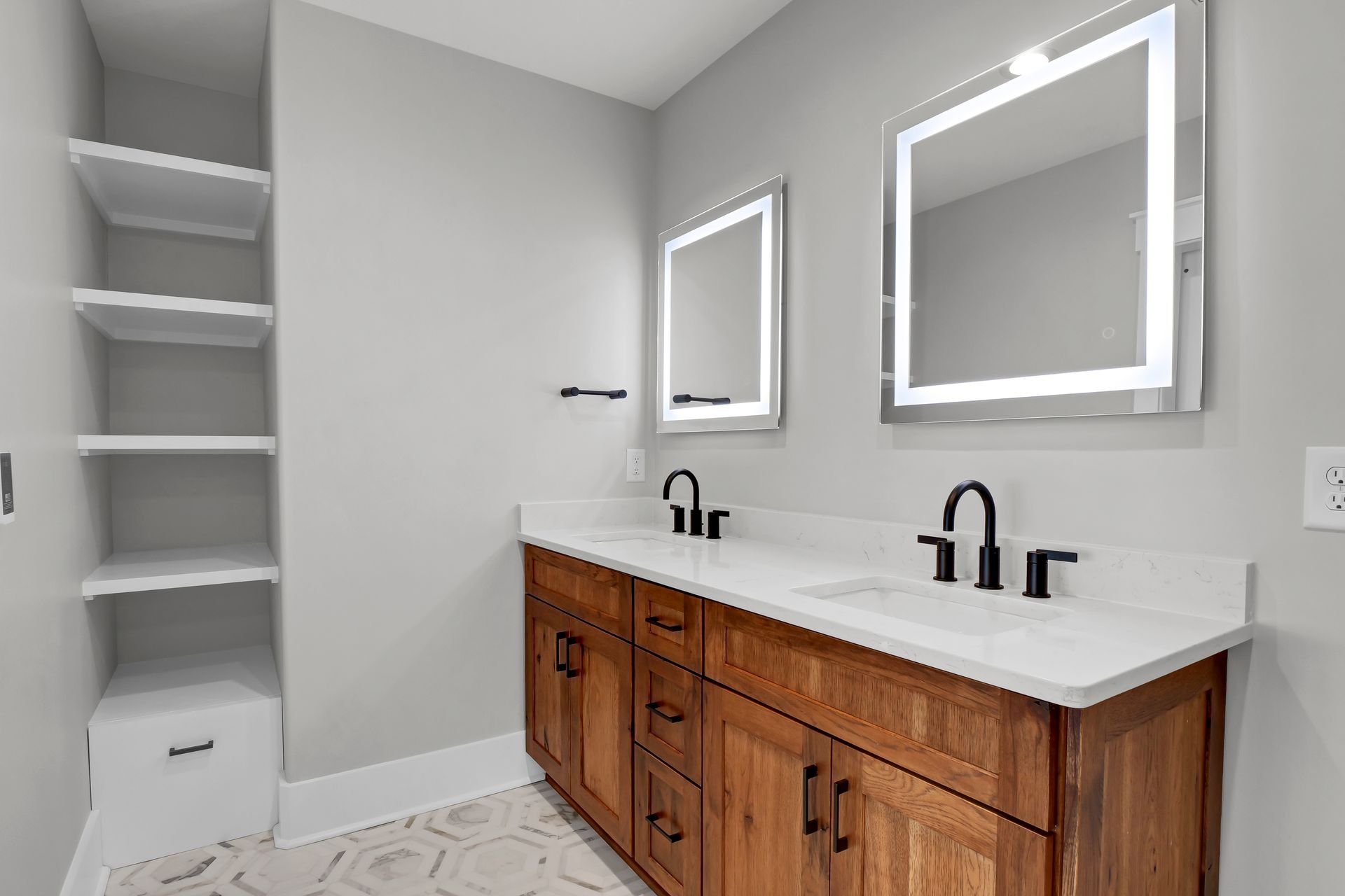 Bathroom with double vanity, two mirrors with lights, open shelving, wood cabinets, and gray walls.
