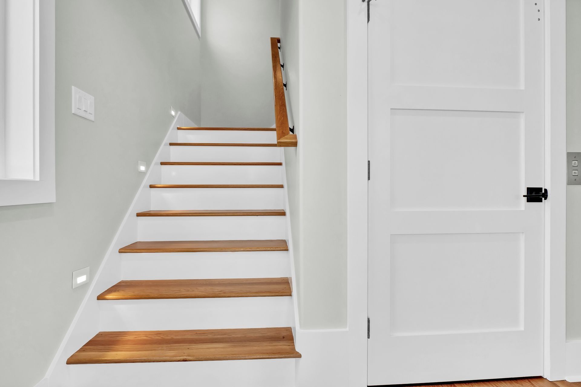 Staircase with wooden steps and white risers, leading upwards next to a white door.