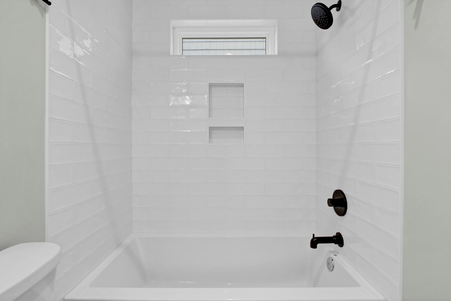 White bathroom with bathtub, black fixtures, and a small window.