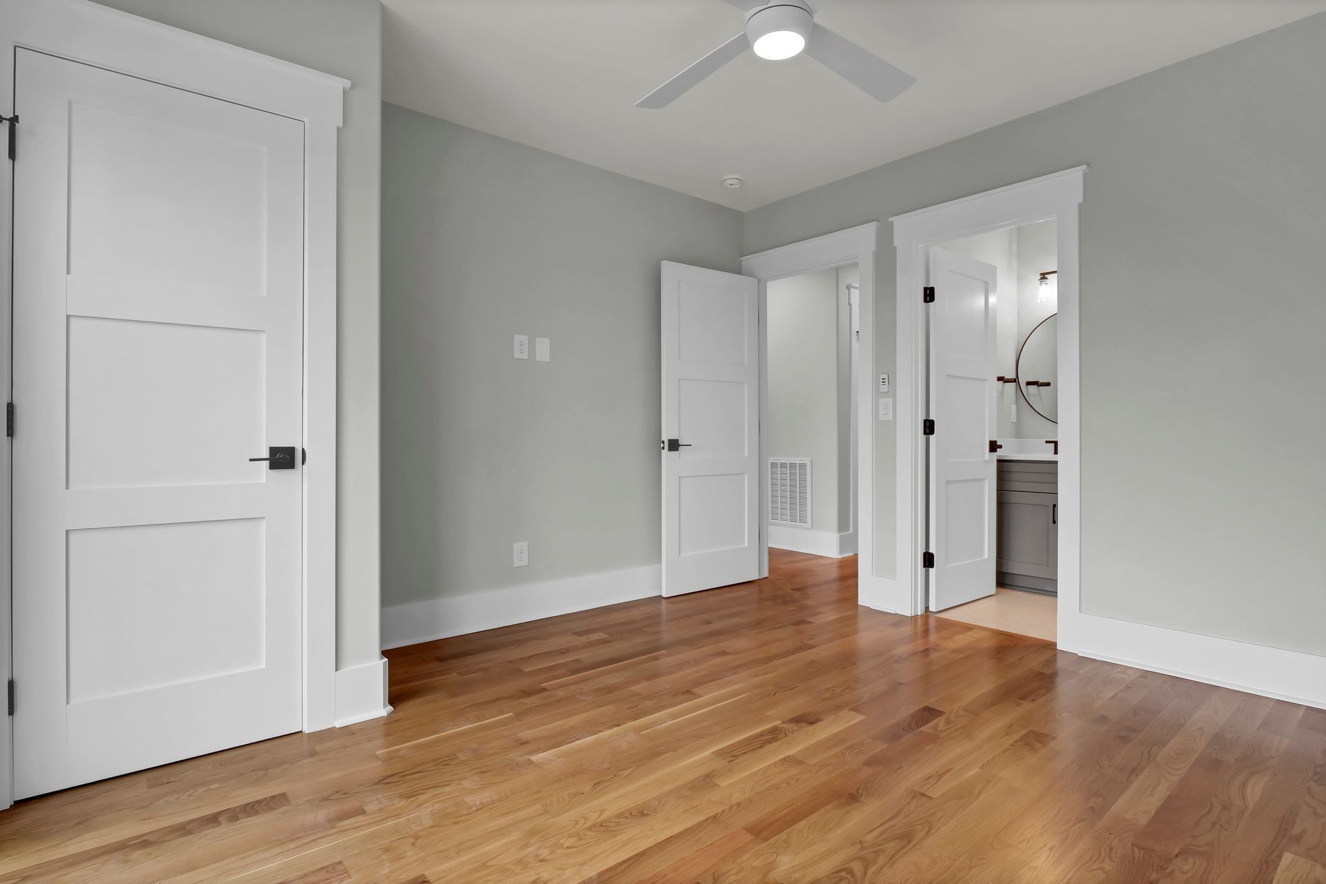 Empty bedroom with hardwood floors, white doors, and light gray walls.