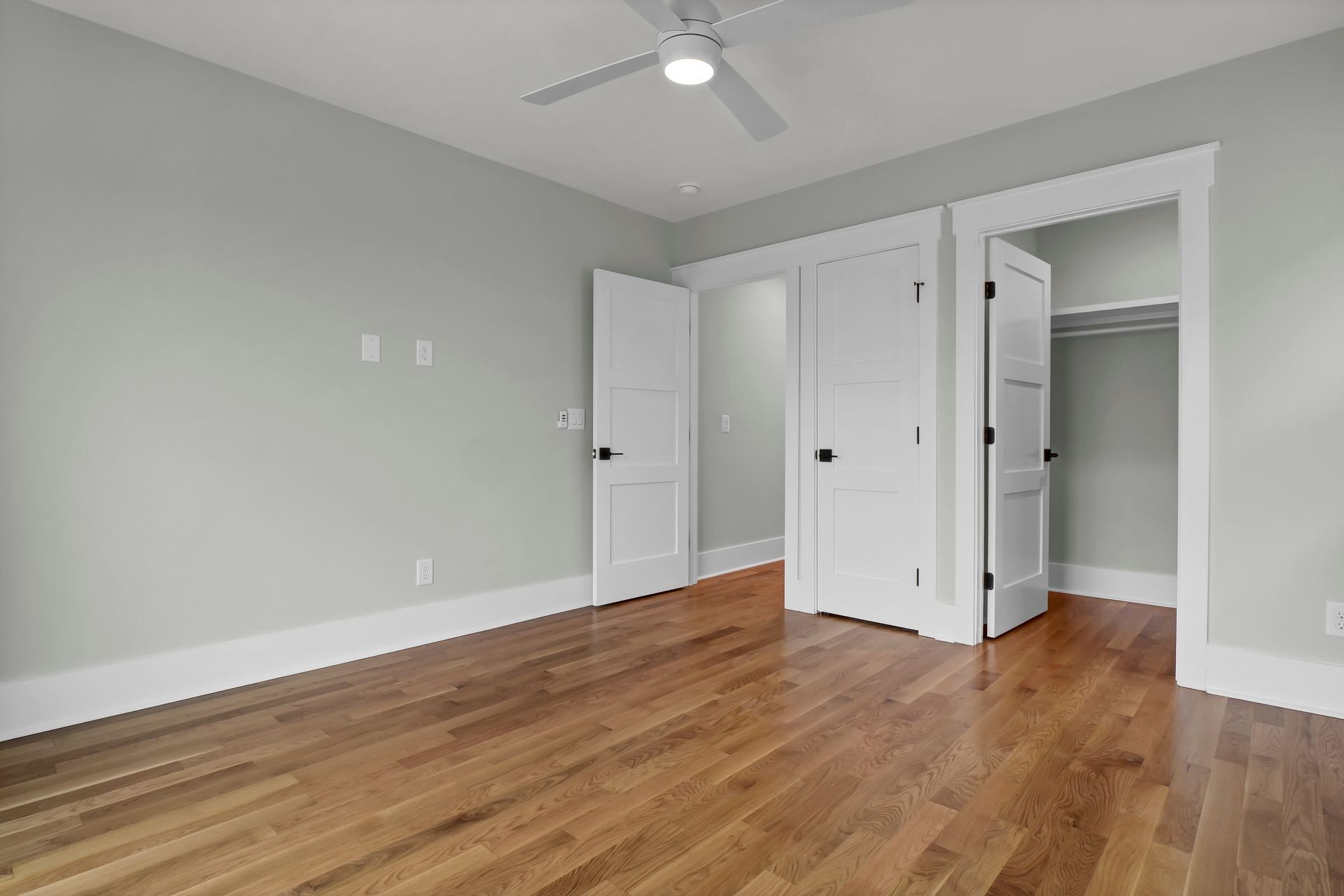 Empty bedroom with hardwood floors, white doors, and a ceiling fan.
