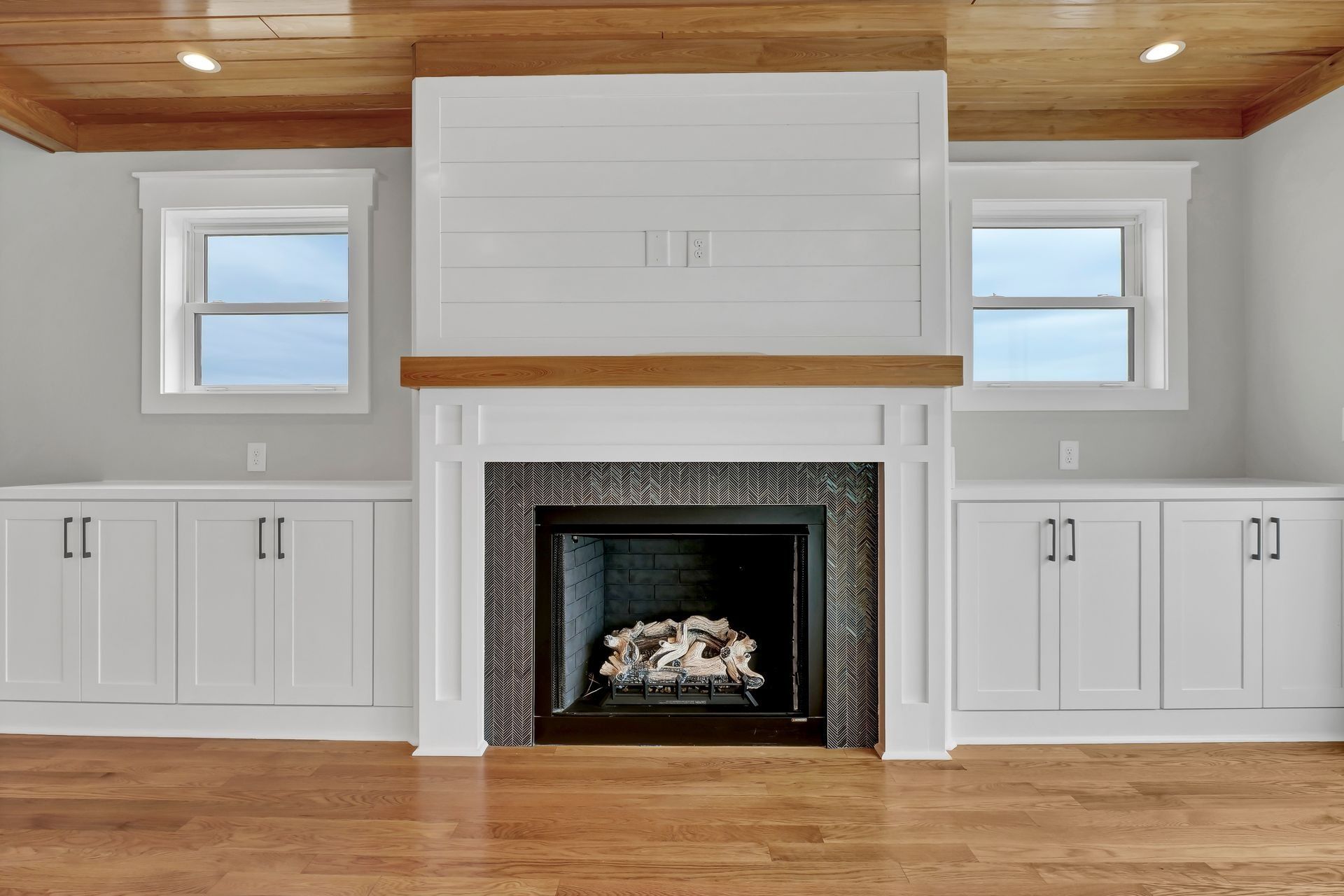 Fireplace with white cabinets, windows, and wood ceiling in a light-colored room.