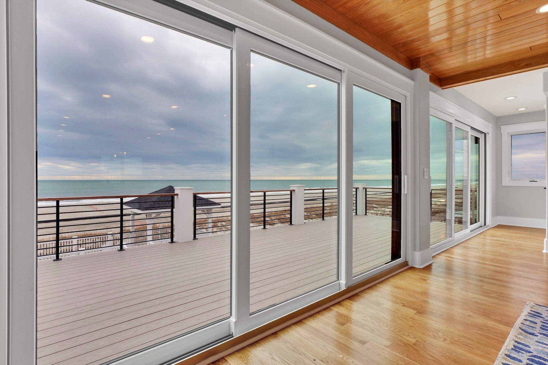 Sliding glass doors open to a deck overlooking a body of water under a cloudy sky.