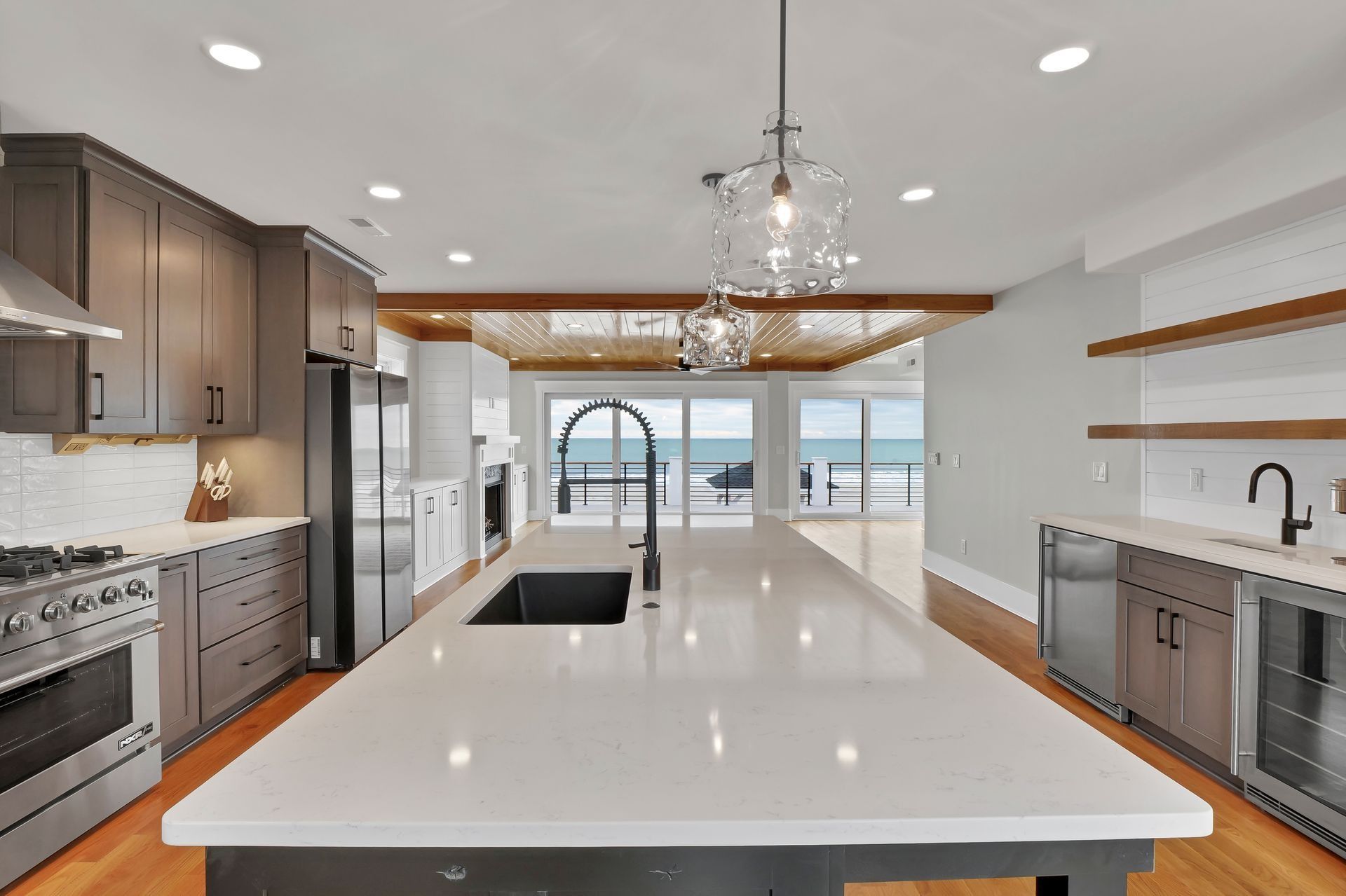 Modern kitchen with large island, ocean view, gray cabinets, stainless steel appliances.