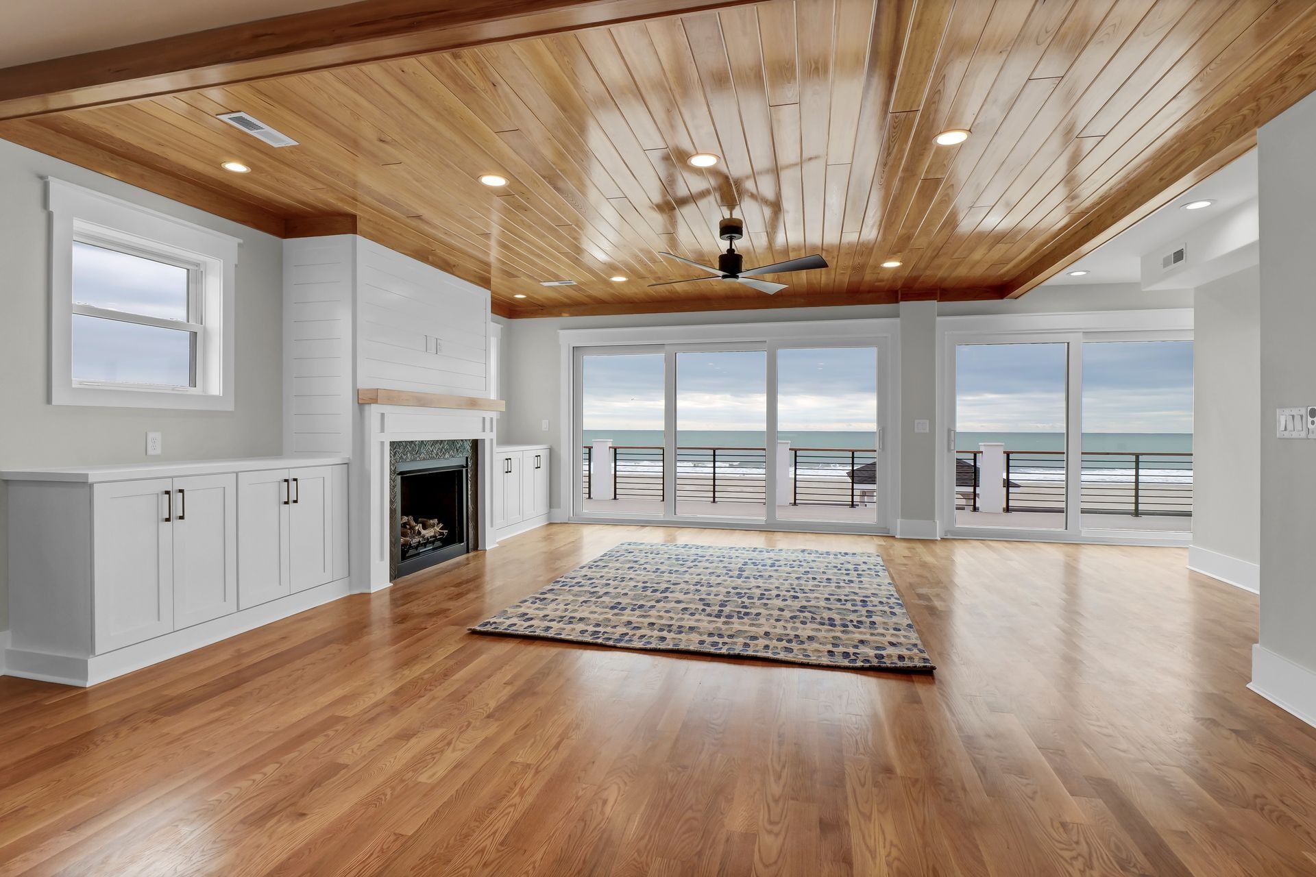 Living room with ocean view, hardwood floors, wood ceiling, white cabinetry, fireplace, and sliding glass doors.