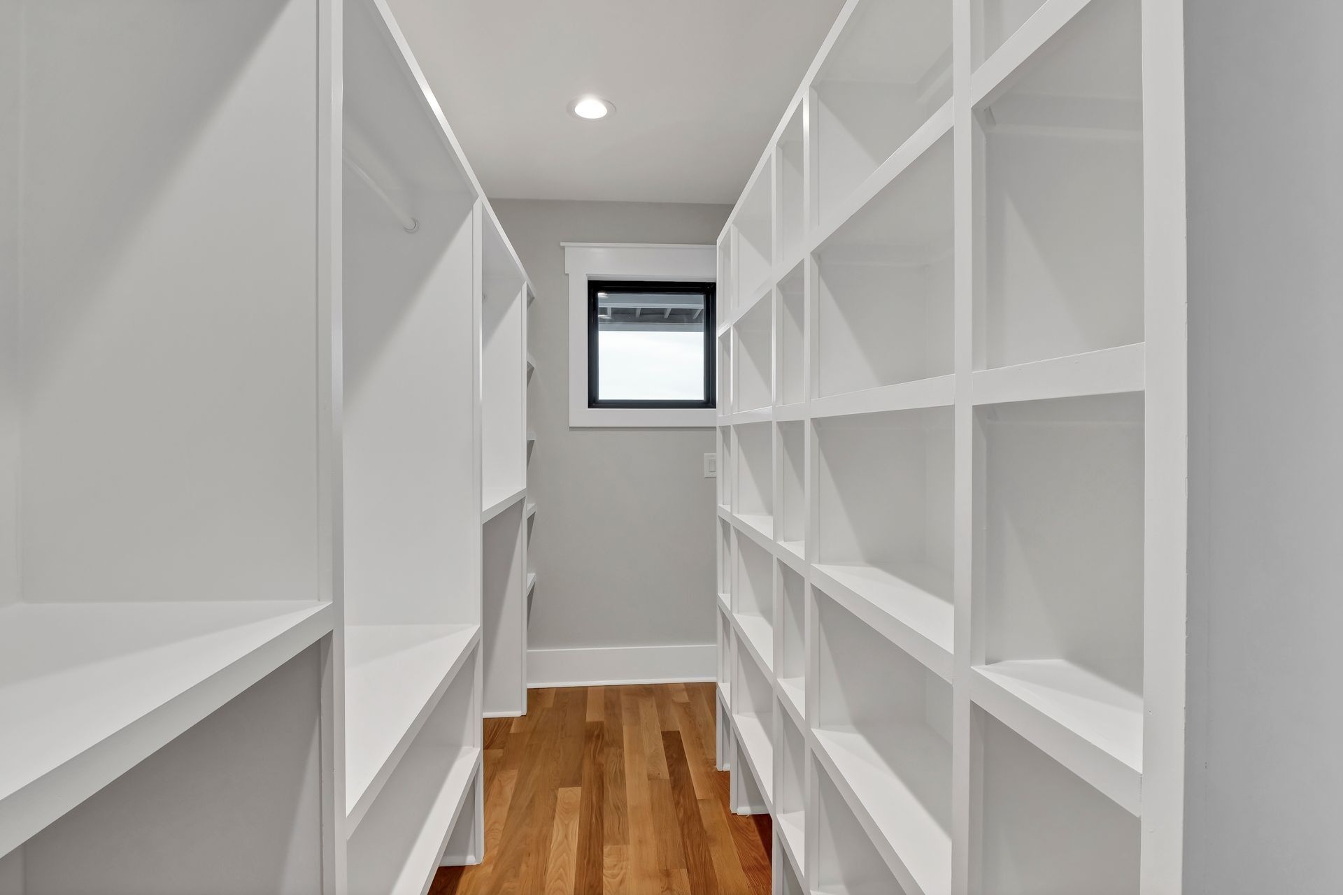 White walk-in closet with grid shelving and hardwood floor, a window at the end.