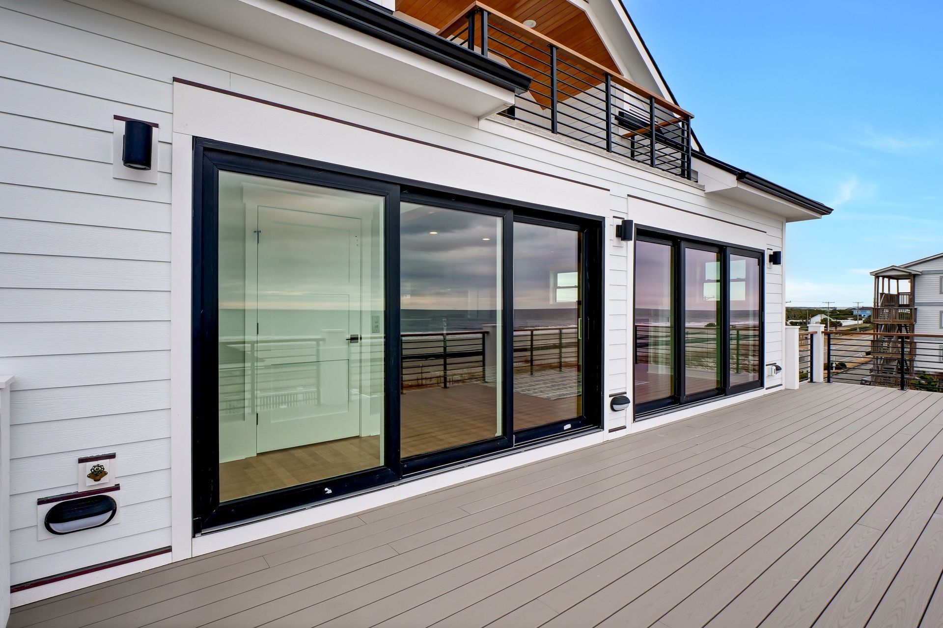 Exterior of a white house with large glass sliding doors and a gray deck overlooking the ocean.