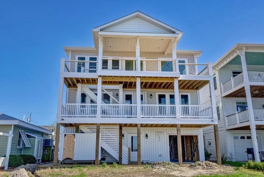Three-story beach house with white siding and decks. Sunny day, clear blue sky.