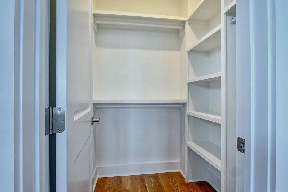 Empty white closet with a rod and shelves, hardwood floor, viewed from the doorway.