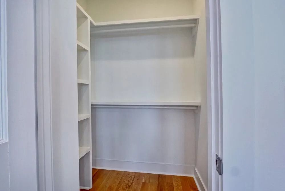 Empty white closet with built-in shelves, a hanging rod, and wood floor.