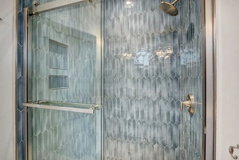 Glass shower enclosure with blue textured tile, silver fixtures, and a glass door.