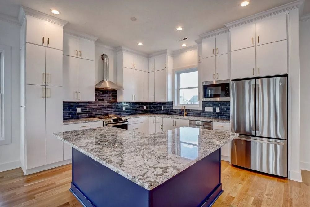 Kitchen with white cabinets, blue island, granite countertop, stainless steel refrigerator.