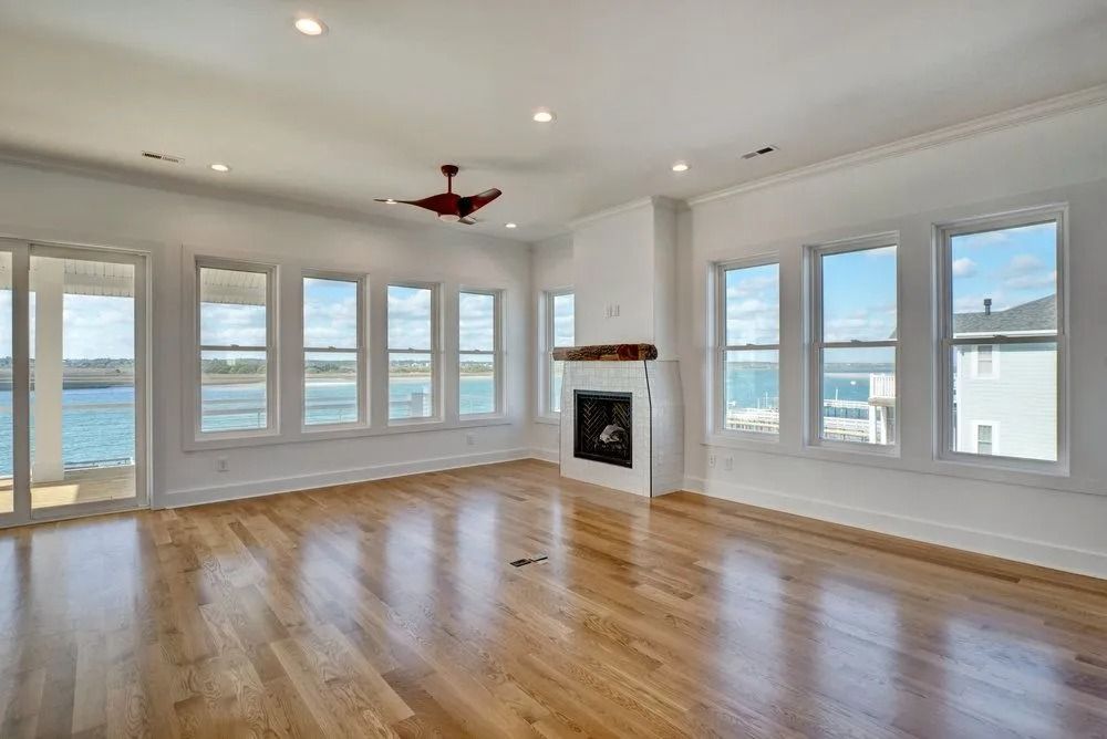 Spacious, bright living room with wood floors, fireplace, and windows overlooking water.