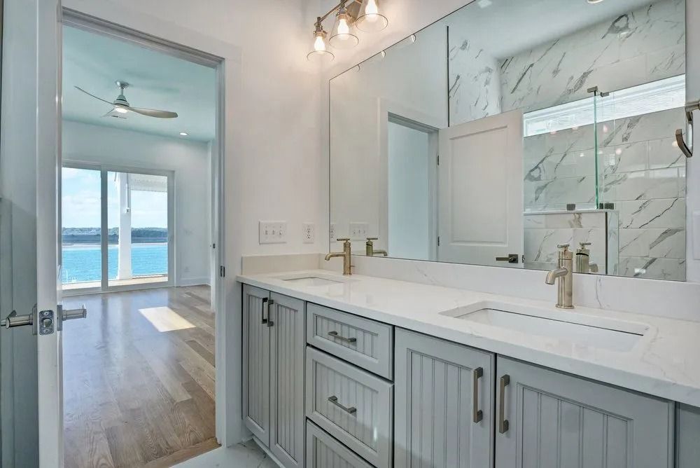 Bathroom with double sink vanity, gray cabinets, white countertop, and view of a room with water view.