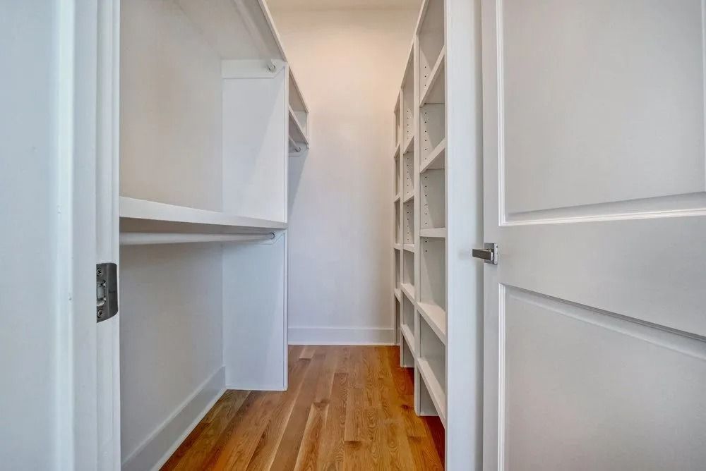 Empty white walk-in closet with shelves and wood floor.