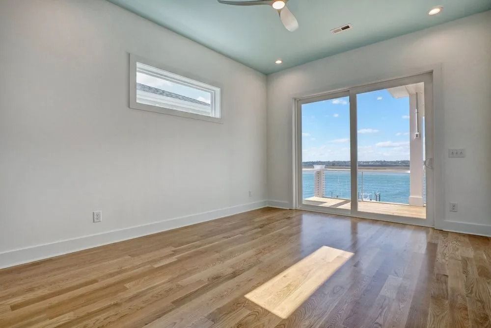 Empty room with wood floor, large glass doors overlooking water, white walls, and a light blue ceiling.