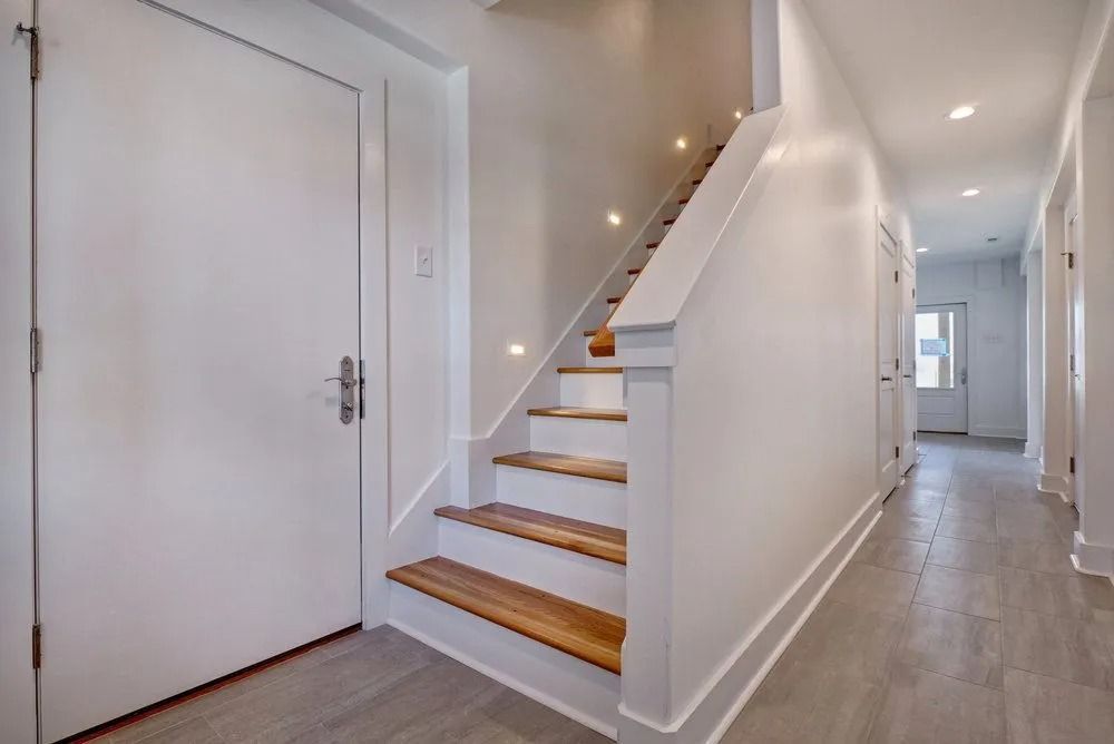 Hallway with wooden stairs, white walls, and a large white door.