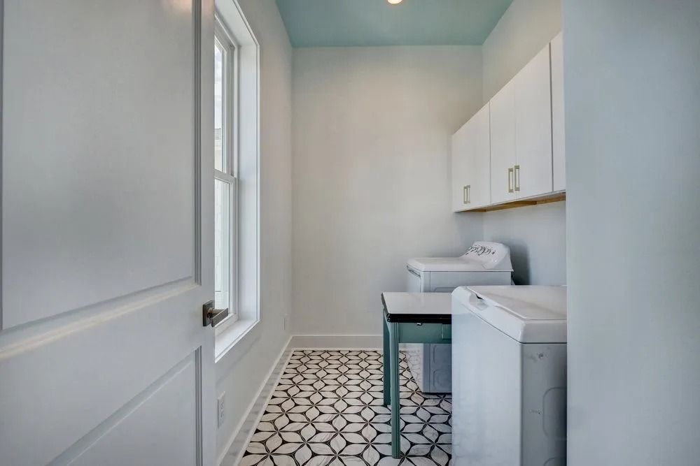 Laundry room with white appliances, cabinets, and a blue ceiling. Black and white patterned floor.