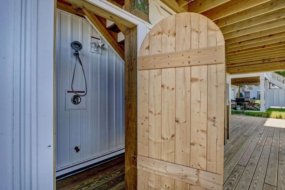 Outdoor wooden shower with an arched wooden door on a wooden deck.
