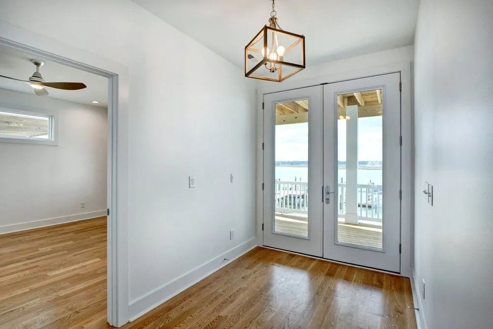Hallway with white walls, wood floors, and French doors leading to a balcony overlooking water.