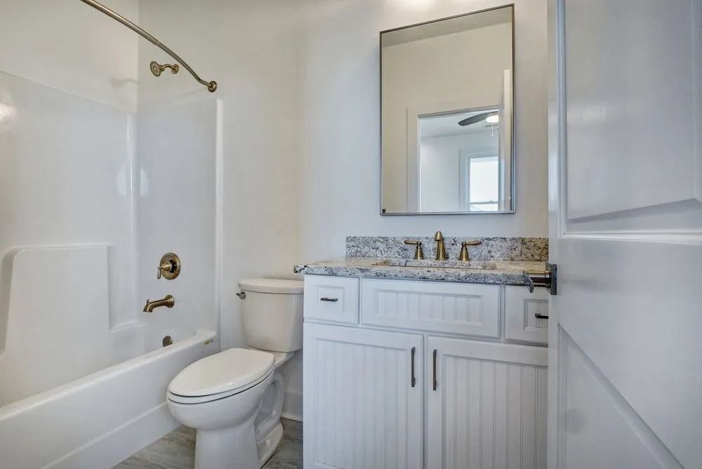 White bathroom with a bathtub, toilet, vanity, and mirror.
